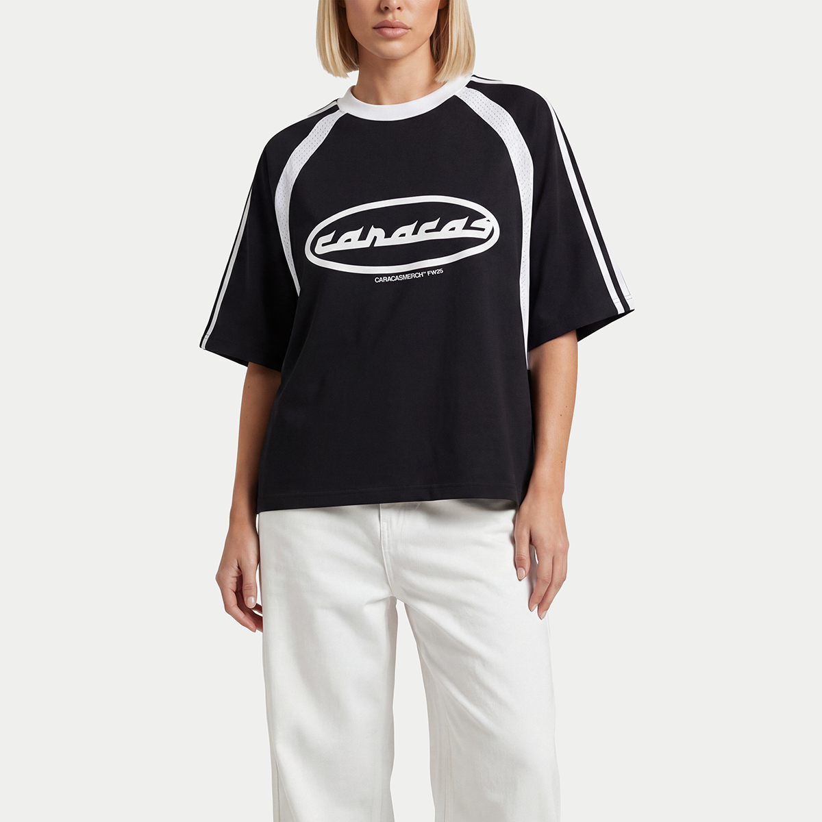 Model wearing the black Caracas boxy jersey by Caracas Merch with white sleeve stripes and cream wide-leg trousers